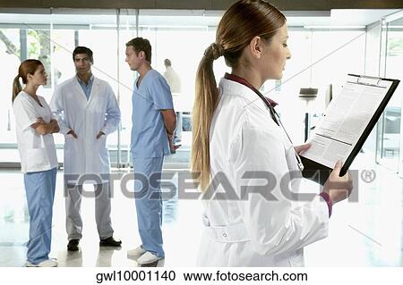 Female doctor reading a medical report with her colleagues discussing in the background View Large Photo Image Stock Image - Female doctor reading a medical report with her colleagues discussing in the background. Fotosearch