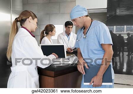 Female doctor using a laptop with a surgeon standing beside her View Large Photo Image Stock Image - Female doctor using a laptop with a surgeon standing beside her. Fotosearch