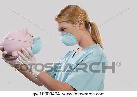 Female doctor wearing a flue mask and holding a piggy bank View Large Photo Image Picture - Female doctor wearing a flue mask and holding a piggy bank. Fotosearch