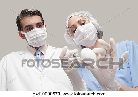 Female lab technician injecting into an egg with her colleague standing beside her View Large Photo Image Stock Image - Female lab technician injecting into an egg with her colleague standing beside her. Fotosearch