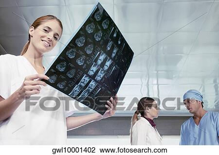 Female nurse examining an X-Ray with her colleagues discussing in the background View Large Photo Image Stock Image - Female nurse examining an X-Ray with her colleagues discussing in the background. Fotosearch