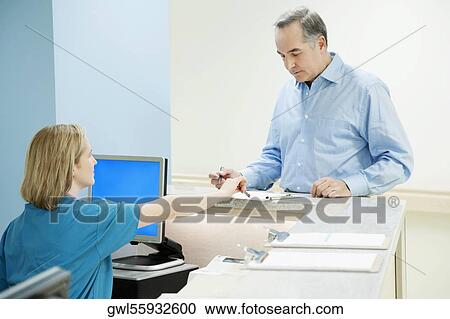 Female nurse helping a patient in filling form at a reception counter in a hospital View Large Photo Image Stock Image - Female nurse helping a patient in filling form at a reception counter in a hospital. Fotosearch