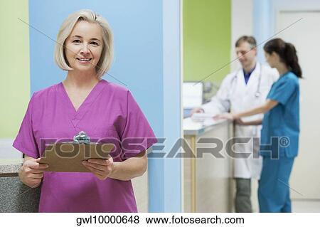 Female nurse holding a clipboard with a doctor and a nurse in the background View Large Photo Image Stock Photo - Female nurse holding a clipboard with a doctor and a nurse in the background. Fotosearch