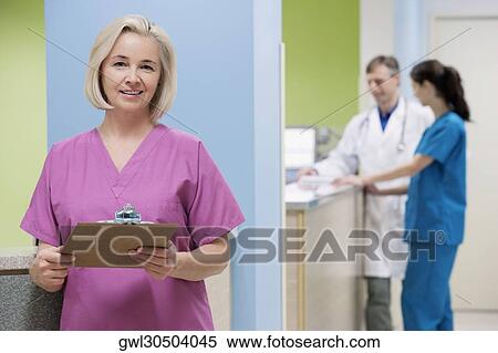 Female nurse holding a clipboard with a doctor and a nurse in the background View Large Photo Image Stock Photography - Female nurse holding a clipboard with a doctor and a nurse in the background. Fotosearch