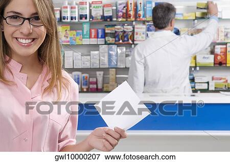 Stock Photo - Female pharmacist holding a prescription and a male pharmacist in the background. Fotosearch