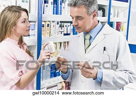 Female pharmacist showing a medicine bottle to a male pharmacist View Large Photo Image Picture - Female pharmacist showing a medicine bottle to a male pharmacist. Fotosearch