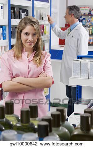 Female pharmacist smiling with a male pharmacist in the background View Large Photo Image Stock Image - Female pharmacist smiling with a male pharmacist in the background. Fotosearch