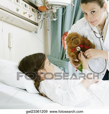 Girl on a hospital bed with a female doctor examining a stuffed toy View Large Photo Image Stock Photo - Girl on a hospital bed with a female doctor examining a stuffed toy. Fotosearch