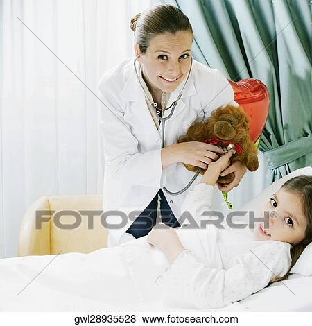 Girl on a hospital bed with a female doctor examining a stuffed toy View Large Photo Image Stock Photo - Girl on a hospital bed with a female doctor examining a stuffed toy. Fotosearch