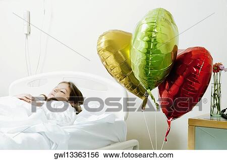 Stock Photograph - Girl with balloons on a hospital bed. Fotosearch