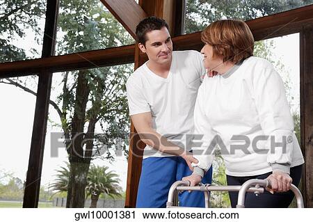 Stock Image - Health worker assisting a disabled woman in a rehabilitation center. Fotosearch