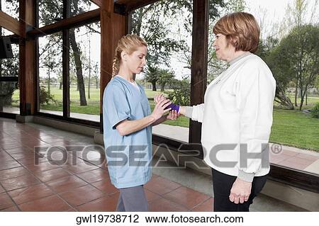 Stock Image - Health worker putting on a wrist brace to a disabled woman. Fotosearch