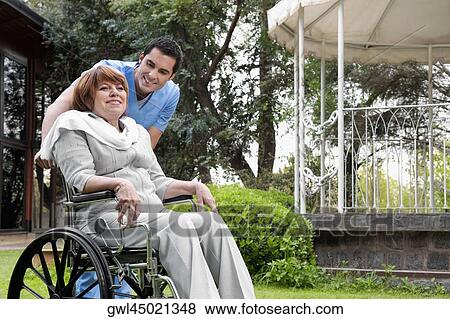 Healthcare worker pushing a woman sitting in a wheelchair View Large Photo Image Stock Photo - Healthcare worker pushing a woman sitting in a wheelchair. Fotosearch