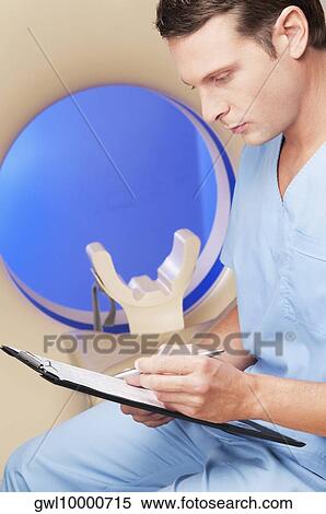 Healthcare worker sitting on a CAT scan machine and writing on a clipboard View Large Photo Image Stock Photography - Healthcare worker sitting on a CAT scan machine and writing on a clipboard. Fotosearch
