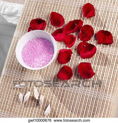 Stock Photograph - High angle view of bath salt and rose petals with shells on a bamboo mat. Fotosearch