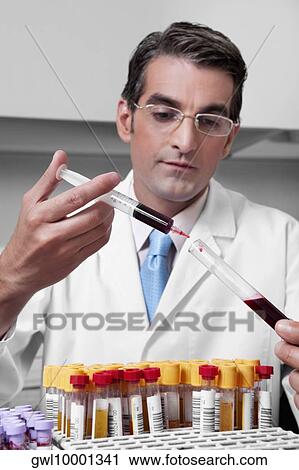 Stock Image - Lab technician filling blood in a test tube from a syringe. Fotosearch
