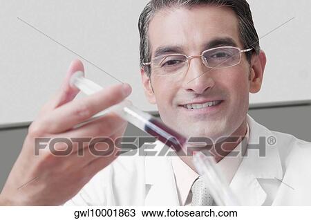 Stock Image - Lab technician filling blood in a test tube from a syringe. Fotosearch