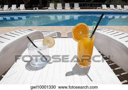 Stock Image - Lounge chairs with juices on table at the poolside. Fotosearch
