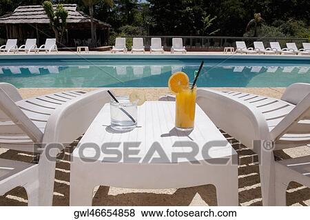 Lounge chairs with juices on table at the poolside View Large Photo Image Stock Photo - Lounge chairs with juices on table at the poolside. Fotosearch