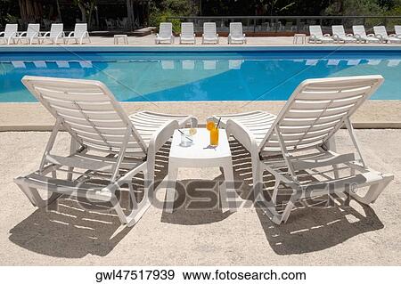 Lounge chairs with juices on table at the poolside View Large Photo Image Stock Photo - Lounge chairs with juices on table at the poolside. Fotosearch