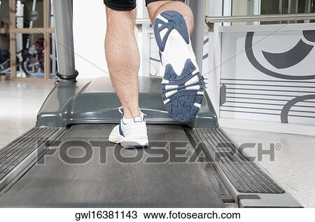 Stock Image - Low section view of a man running on a treadmill. Fotosearch