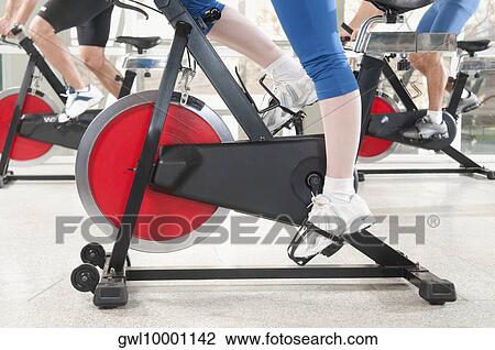 Stock Image - Low section view of three people working out on exercise bikes. Fotosearch