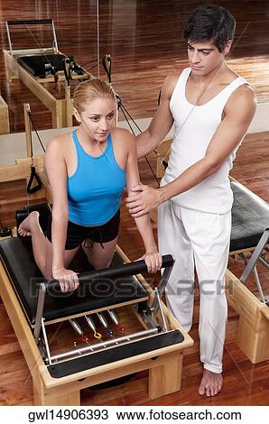 Stock Image - Male instructor assisting a woman in a gym. Fotosearch
