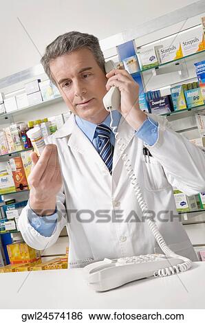 Male pharmacist holding a medicine bottle and talking on the telephone View Large Photo Image Stock Photograph - Male pharmacist holding a medicine bottle and talking on the telephone. Fotosearch
