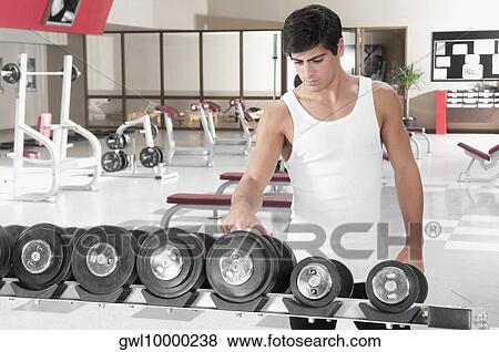 Stock Photo - Man choosing dumbbells in a gym. Fotosearch