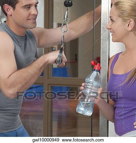 Man exercising in a gym with a woman smiling beside him View Large Photo Image Stock Photo - Man exercising in a gym with a woman smiling beside him. Fotosearch