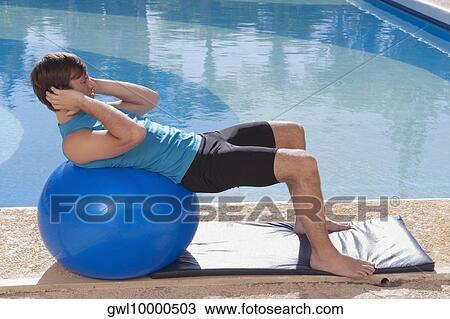 Stock Image - Man exercising with a fitness ball at the poolside. Fotosearch