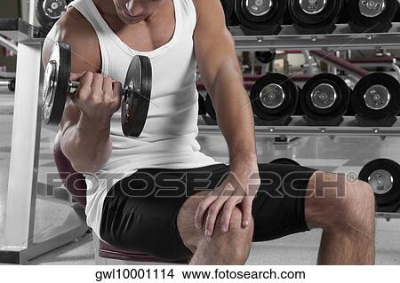 Man exercising with dumbbells in a gym View Large Photo Image Picture - Man exercising with dumbbells in a gym. Fotosearch