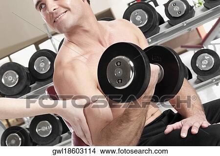 Man exercising with dumbbells in a gym View Large Photo Image Picture - Man exercising with dumbbells in a gym. Fotosearch