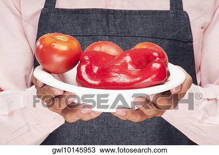 Stock Image - Man holding a plate of red bell peppers and tomatoes. Fotosearch