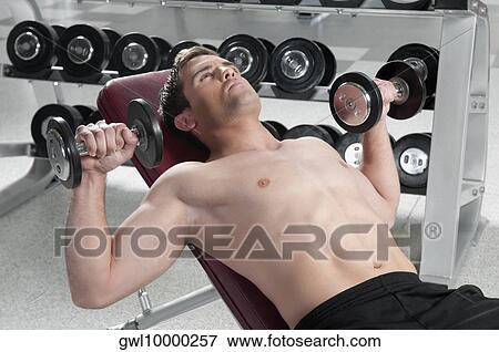 Man lying on a weight bench and exercising with dumbbells View Large Photo Image Stock Photo - Man lying on a weight bench and exercising with dumbbells. Fotosearch
