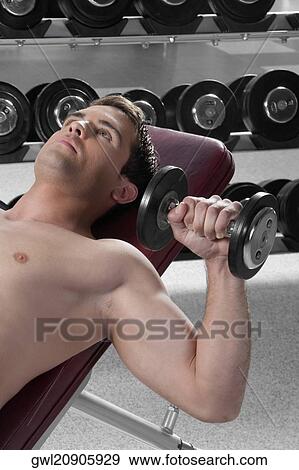 Man lying on a weight bench and exercising with dumbbells View Large Photo Image Stock Photo - Man lying on a weight bench and exercising with dumbbells. Fotosearch