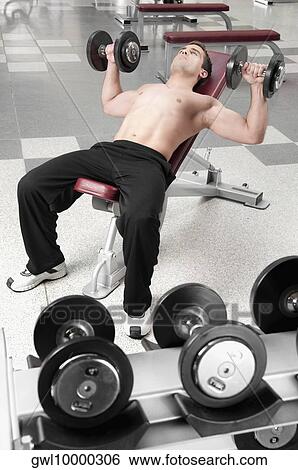 Man lying on a weight bench and exercising with dumbbells View Large Photo Image Stock Photograph - Man lying on a weight bench and exercising with dumbbells. Fotosearch
