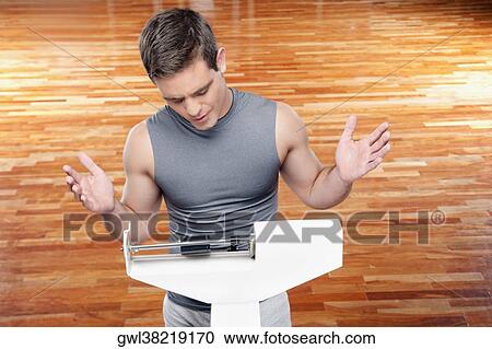 Stock Image - Man measuring his weight on a weighing scale. Fotosearch