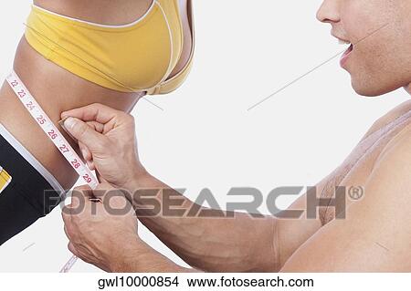 Picture - Man measuring the waist of a woman with a tape measure. Fotosearch