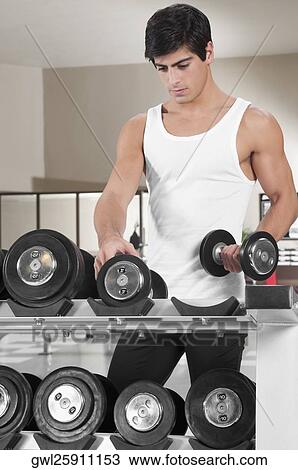 Man picking up dumbbells in a gym View Large Photo Image Stock Image - Man picking up dumbbells in a gym. Fotosearch