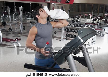 Stock Photo - Man wiping his face with a towel on a treadmill. Fotosearch