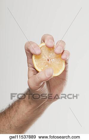 Stock Photo - Man's hand squeezing an orange half. Fotosearch