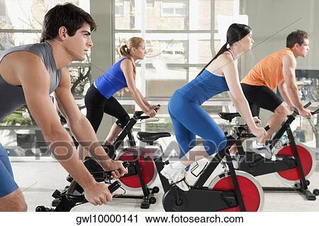 Stock Image - Men and women working out on exercise bikes in a gym. Fotosearch