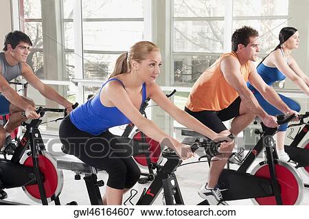 Stock Photo - Men and women working out on exercise bikes in a gym. Fotosearch