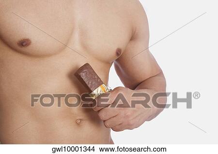 Picture - Mid section view of a man holding a protein bar. Fotosearch