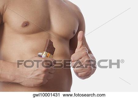 Stock Image - Mid section view of a man holding a protein bar and showing thumbs up sign. Fotosearch