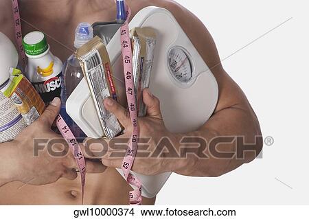 Mid section view of a man holding food supplements and a bathroom scale View Large Photo Image Picture - Mid section view of a man holding food supplements and a bathroom scale. Fotosearch