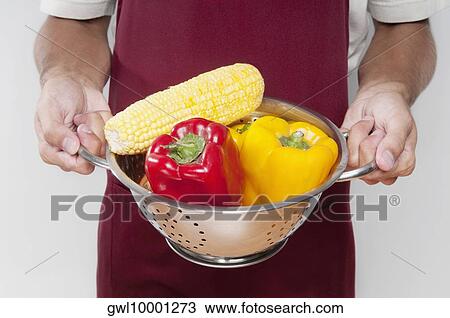Stock Image - Mid section view of a man holding vegetables in a strainer. Fotosearch