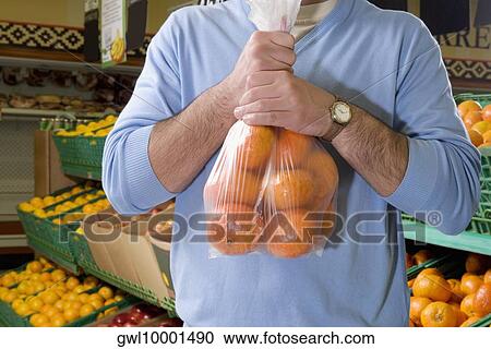 Mid section view of a man holding oranges in a supermarket View Large Photo Image Stock Image - Mid section view of a man holding oranges in a supermarket. Fotosearch
