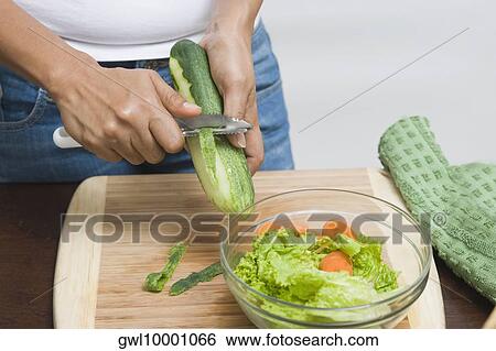 Stock Photograph - Mid section view of a woman peeling a cucumber. Fotosearch